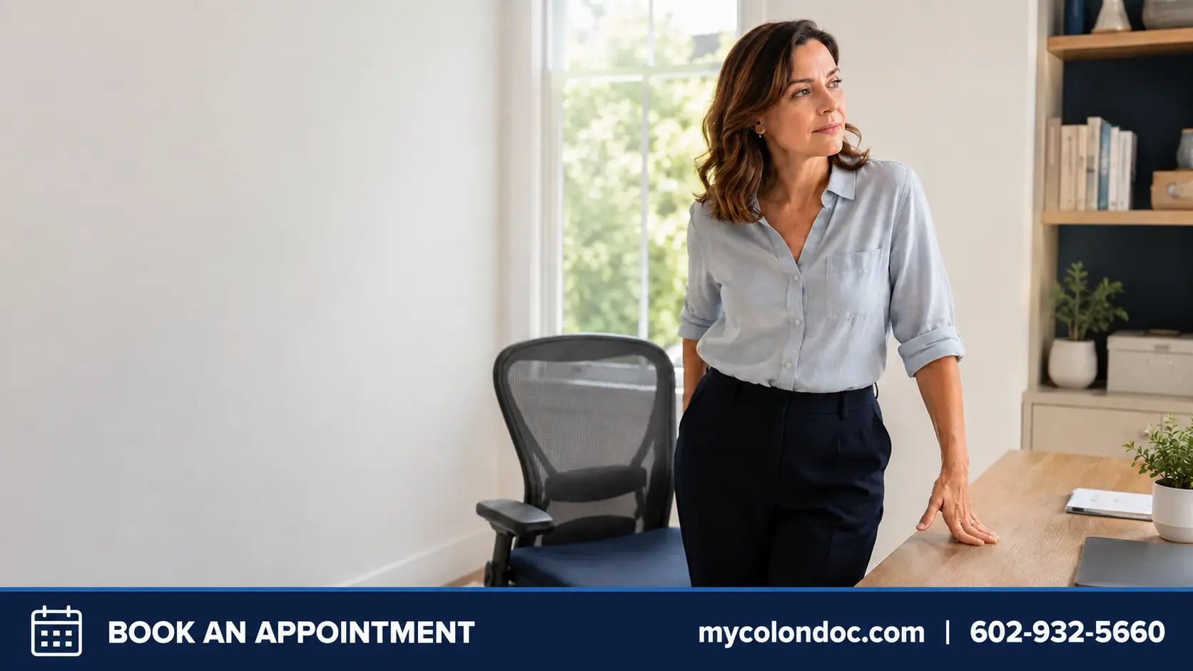 Woman standing beside an office chair because sitting is uncomfortable, illustrating persistent hemorrhoid symptoms.